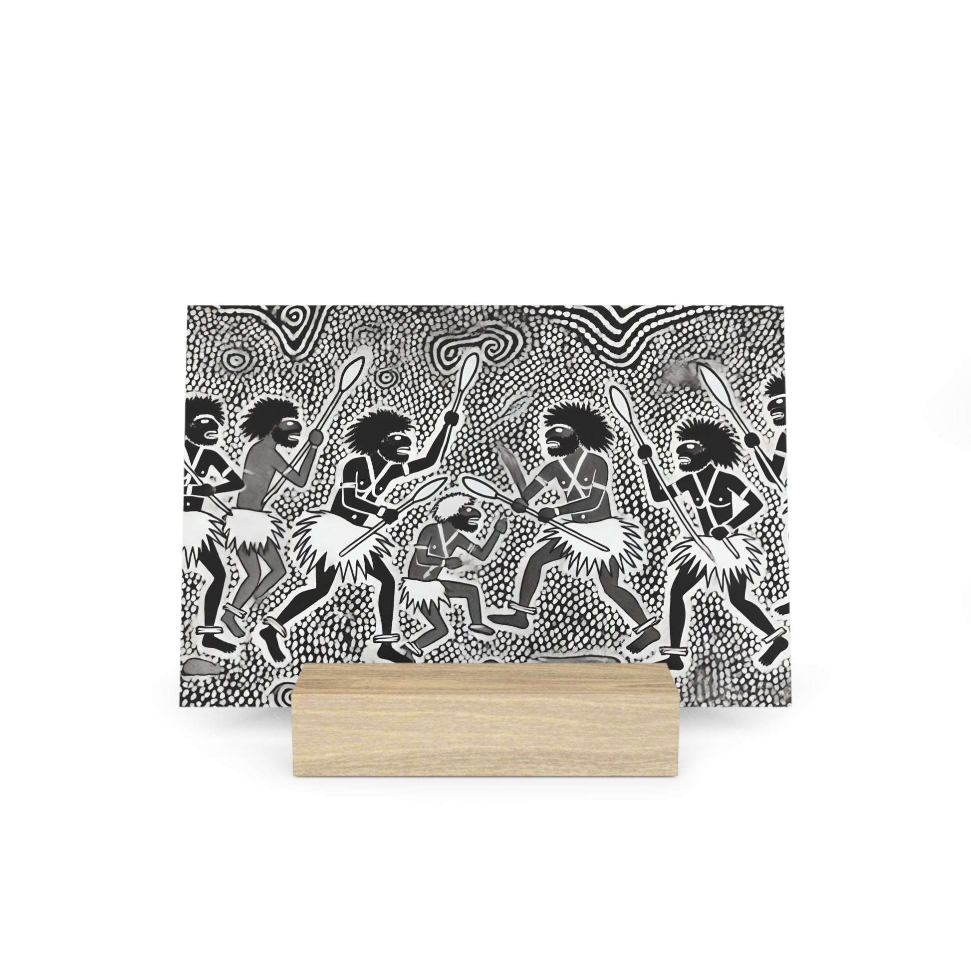 Black-and-white patterned illustration of tribal dancers with spears, mounted on a light wood block base.