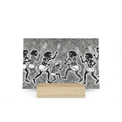 Black-and-white patterned illustration of tribal dancers with spears, mounted on a light wood block base.