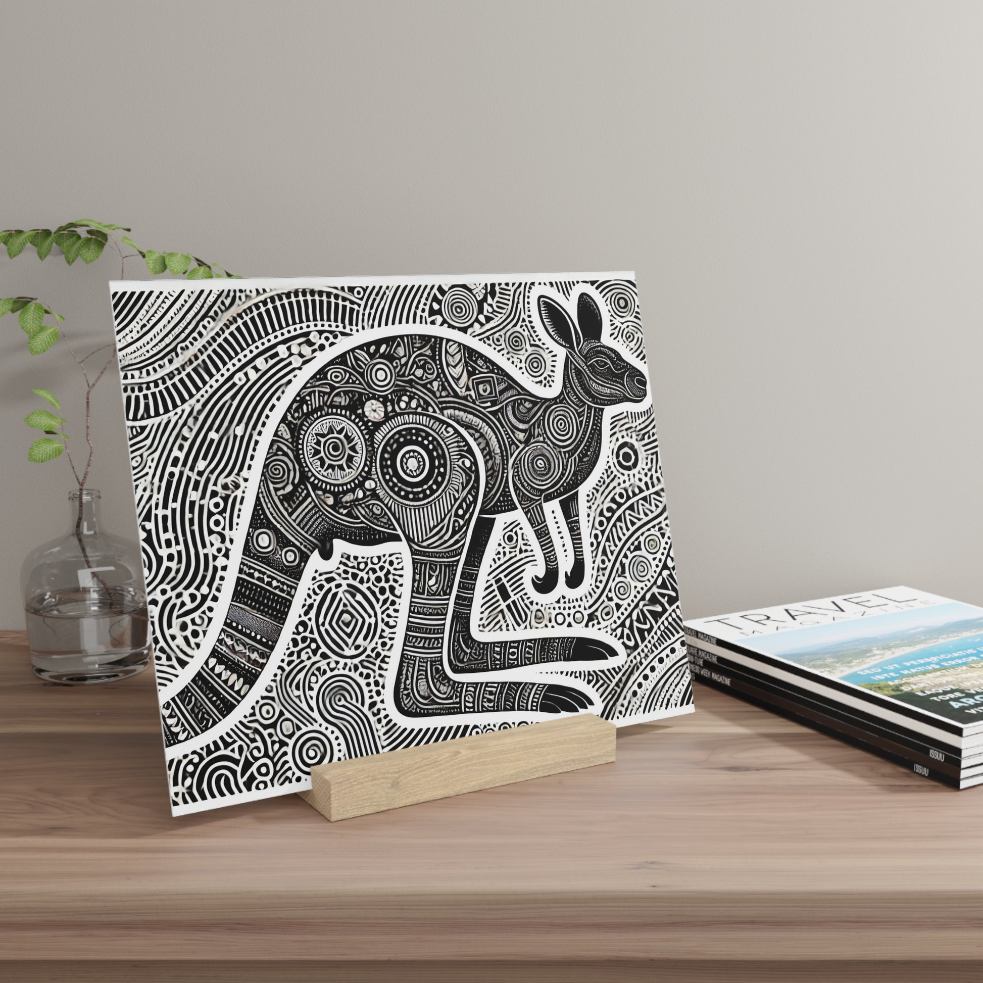 Black-and-white intricate rabbit illustration on canvas, propped on a wooden block on a wood table beside magazines.
