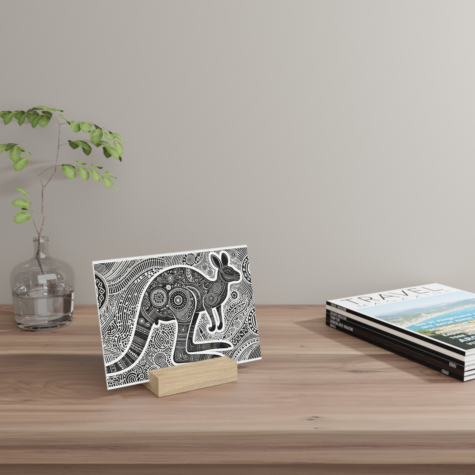 A black-and-white intricately patterned card featuring a rabbit sits on a small wooden stand on a light wood desk beside a glass vase and