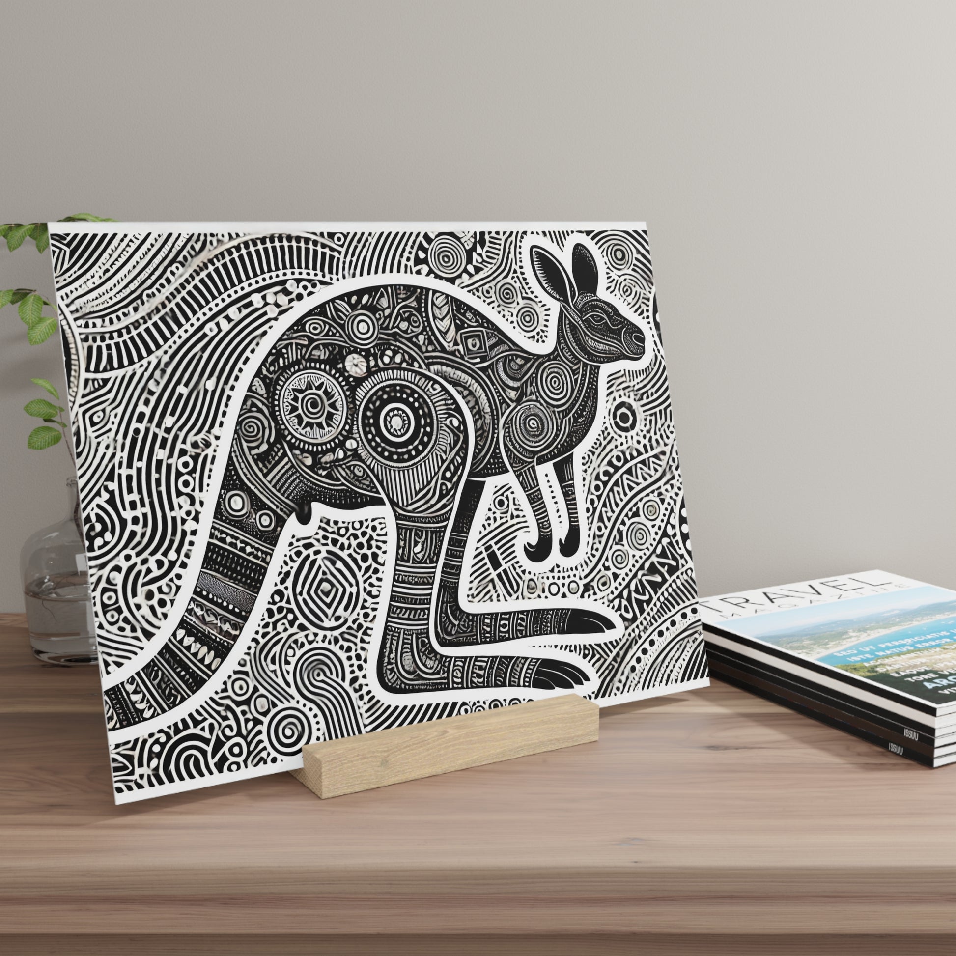 Canvas print of a black-and-white, highly patterned rabbit illustration, propped on a wooden stand beside travel magazines.