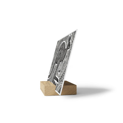 Black-and-white abstract patterned card upright in a light wooden block display against a white background.