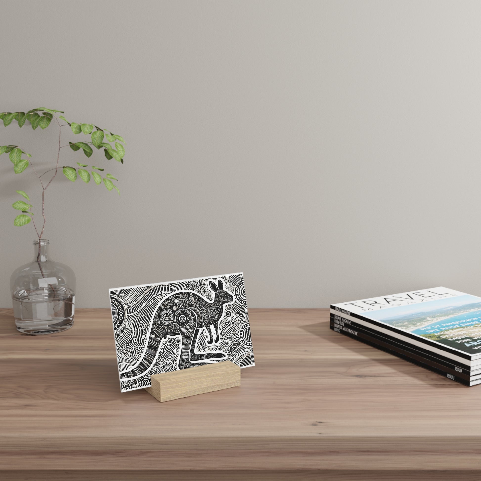 A black-and-white patterned card on a small wooden stand sits on a light wooden desk, with a glass vase and travel magazines nearby.