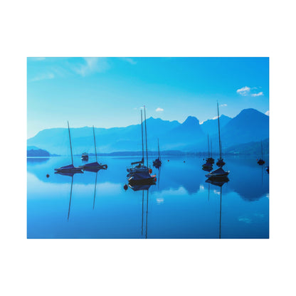Calm blue lake with several sailboats anchored, their masts reflected on the water, against distant blue mountains.