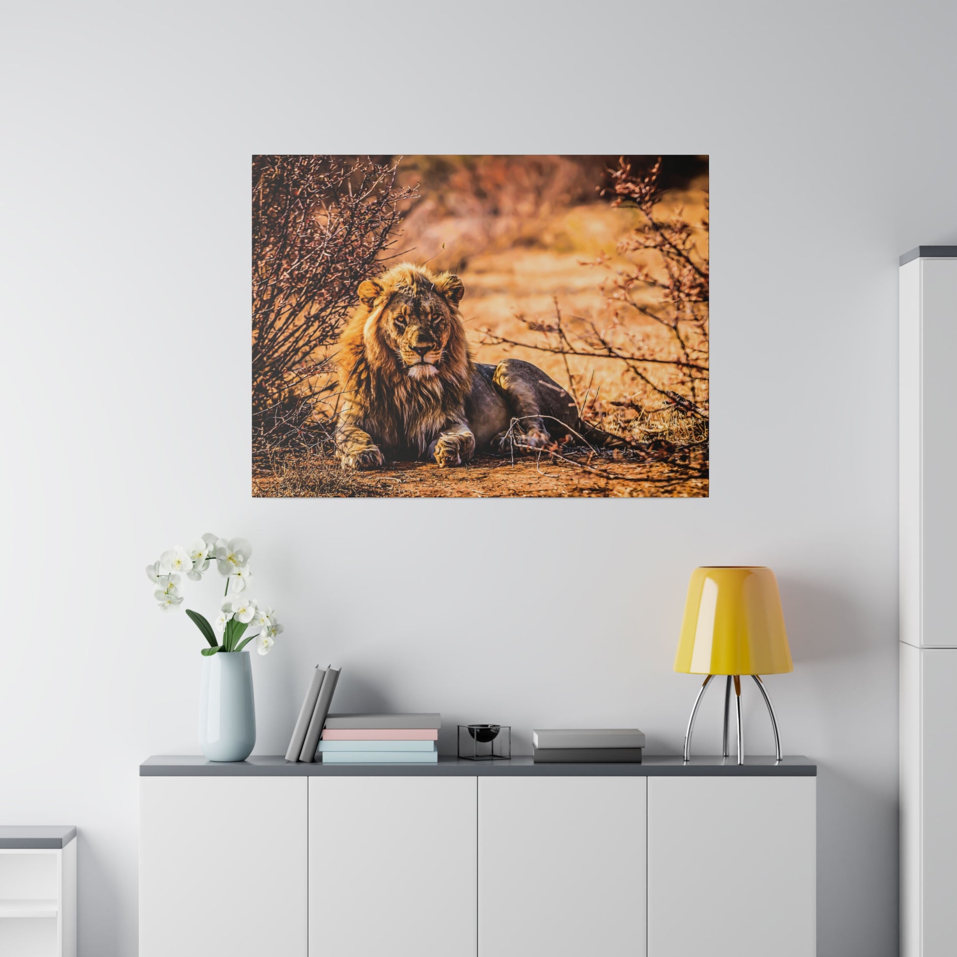 A lion lying in the dry bush, with branches and warm sunlight creating a serene natural setting. The lion's majestic mane and calm demeanor showcase its strength.