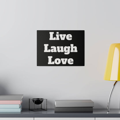 Black wall art with white Live Laugh Love text above a shelf holding pastel books, a small black metal bowl, and a yellow lamp.
