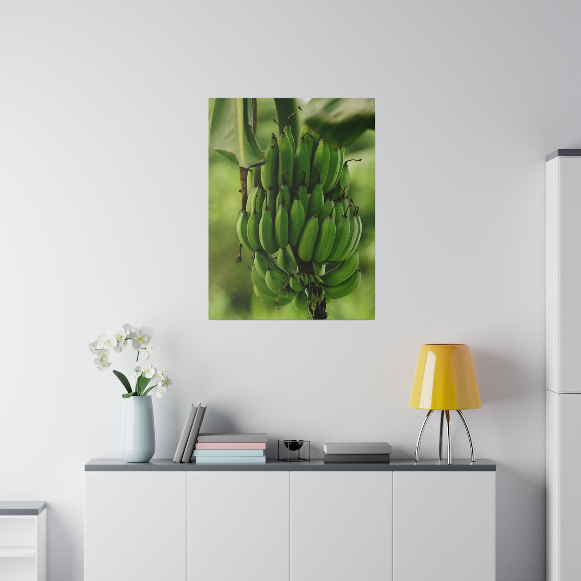 Vertical poster of a large bunch of green bananas on a banana plant, mounted on a white wall above a gray-topped white cabinet.