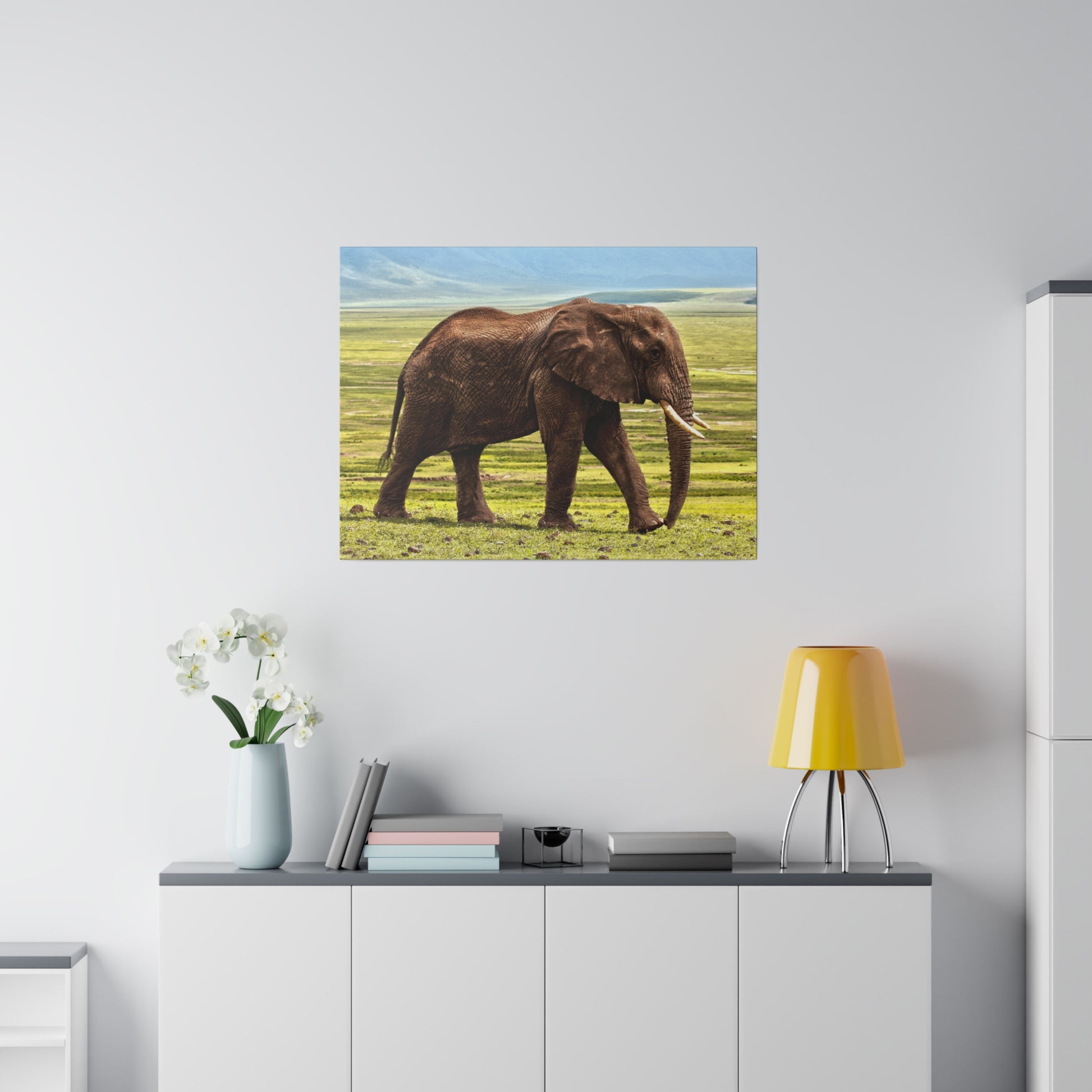 Framed wall art showing a brown African elephant walking on grassy savanna, hung on a white wall.