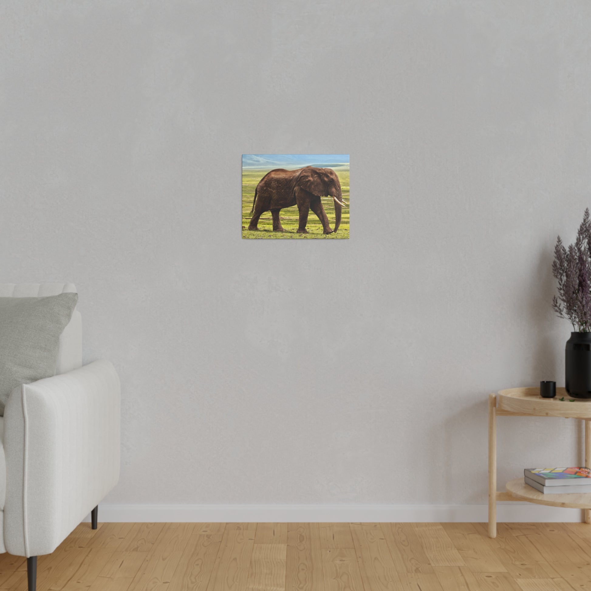 Small canvas painting of a brown African elephant walking on green grass hung on a light gray wall.