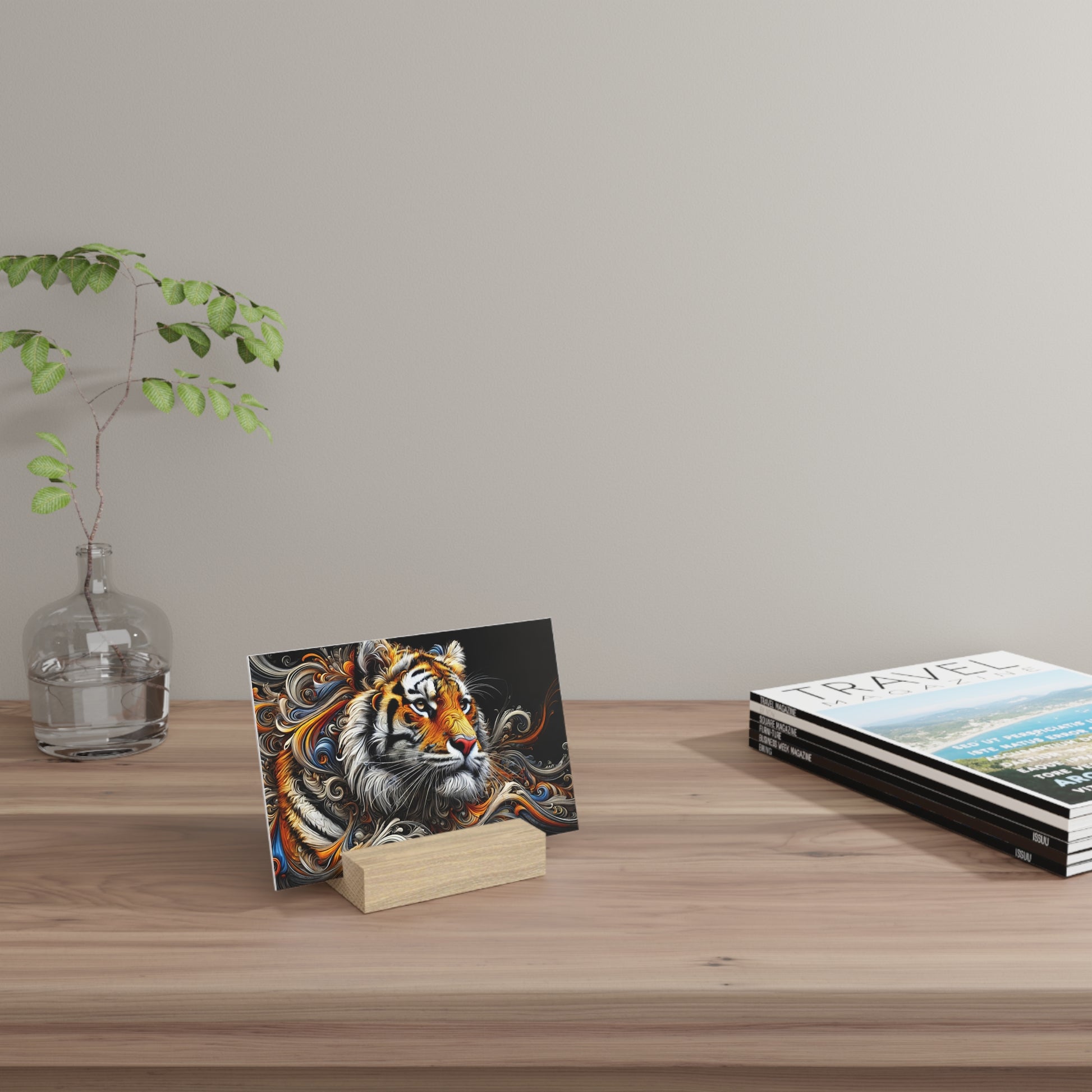 Colorful tiger illustration card on a small wooden block stand, placed on a light wood desk with a glass vase and travel magazines.