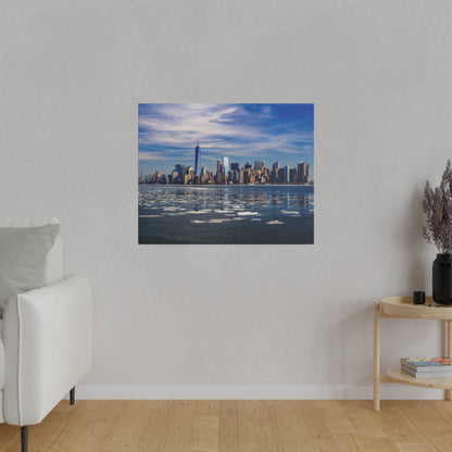 Image shows the Manhattan skyline across an icy river, with scattered ice floes in the foreground and a blue sky.