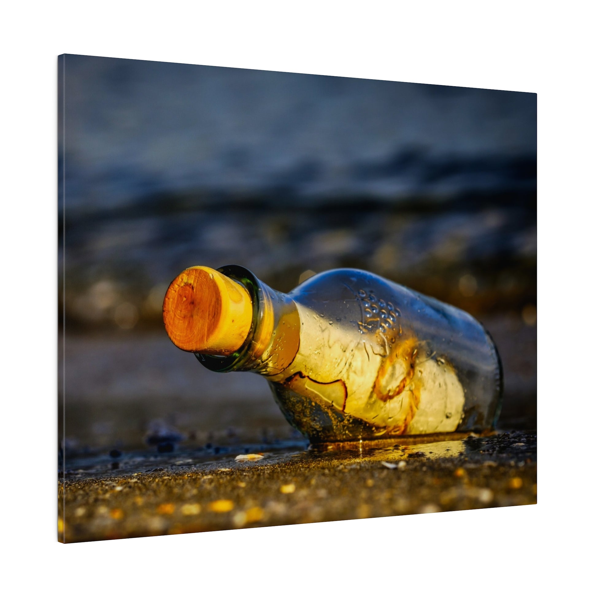 A clear glass bottle with an orange cork rests on wet beach sand, glistening in sunset light.