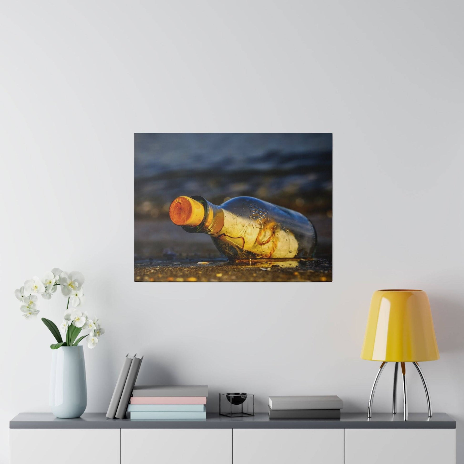 A glass bottle with an orange cap lies on wet sand at the beach, photographed up close, mounted on a white wall.