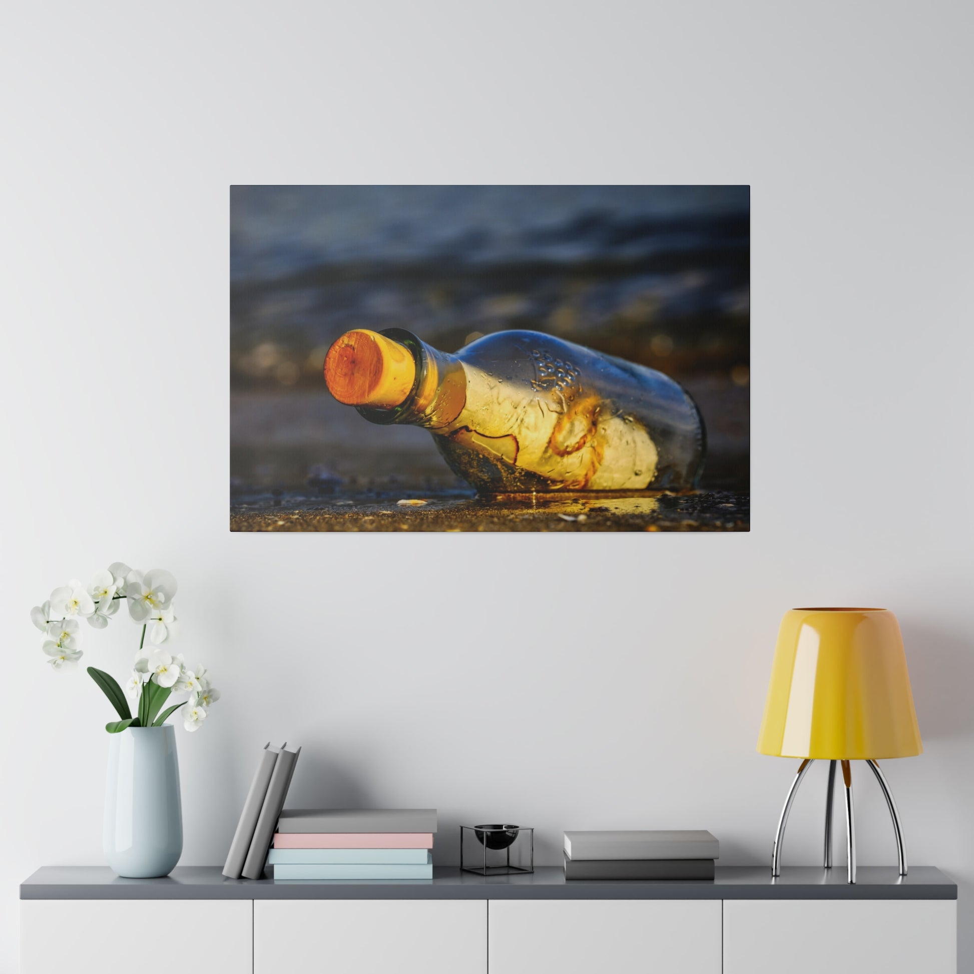 A clear glass bottle with an orange cap lies on wet sand at the beach shoreline.