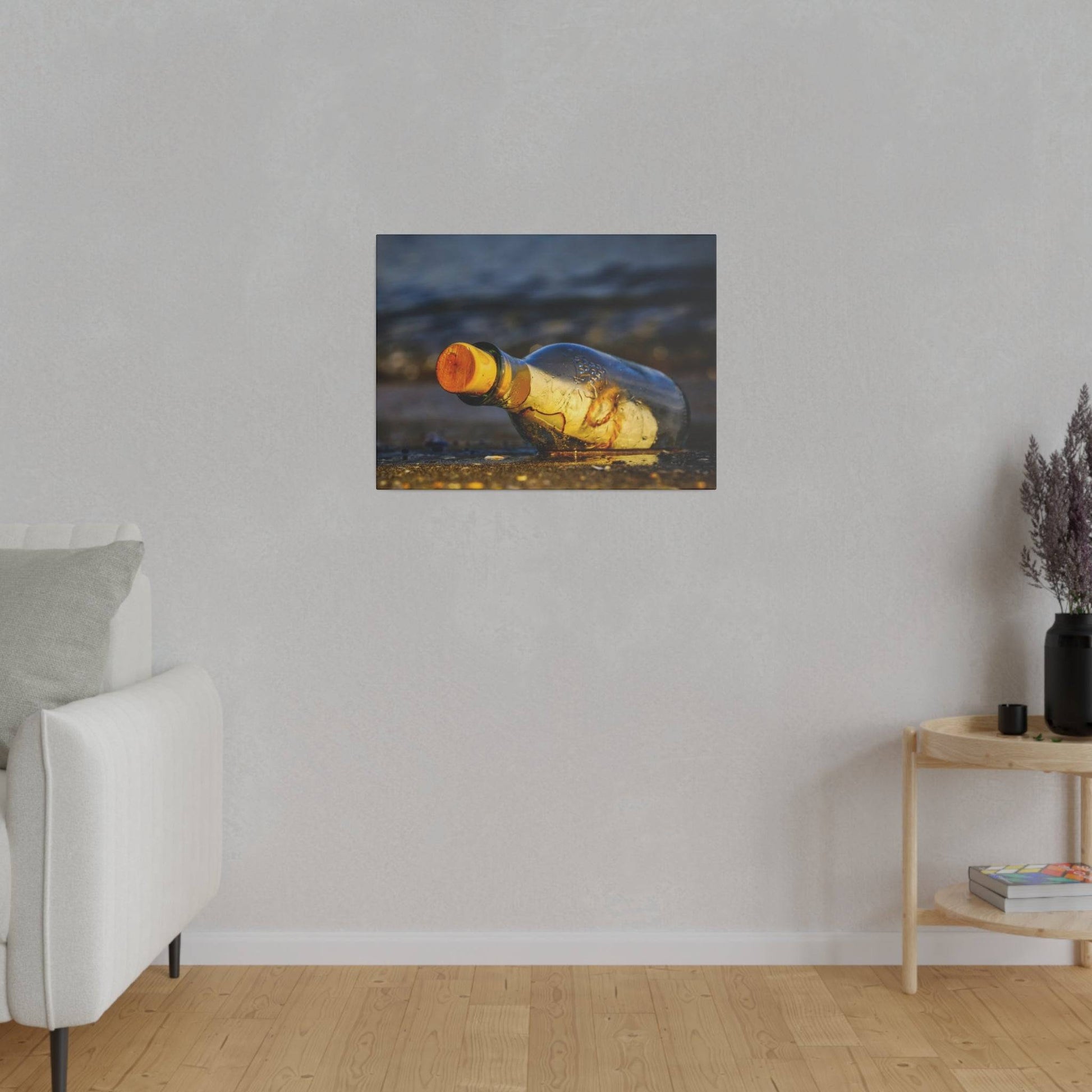 Small wall art print showing a yellow glass bottle lying on sand, hung on a light gray living room wall.