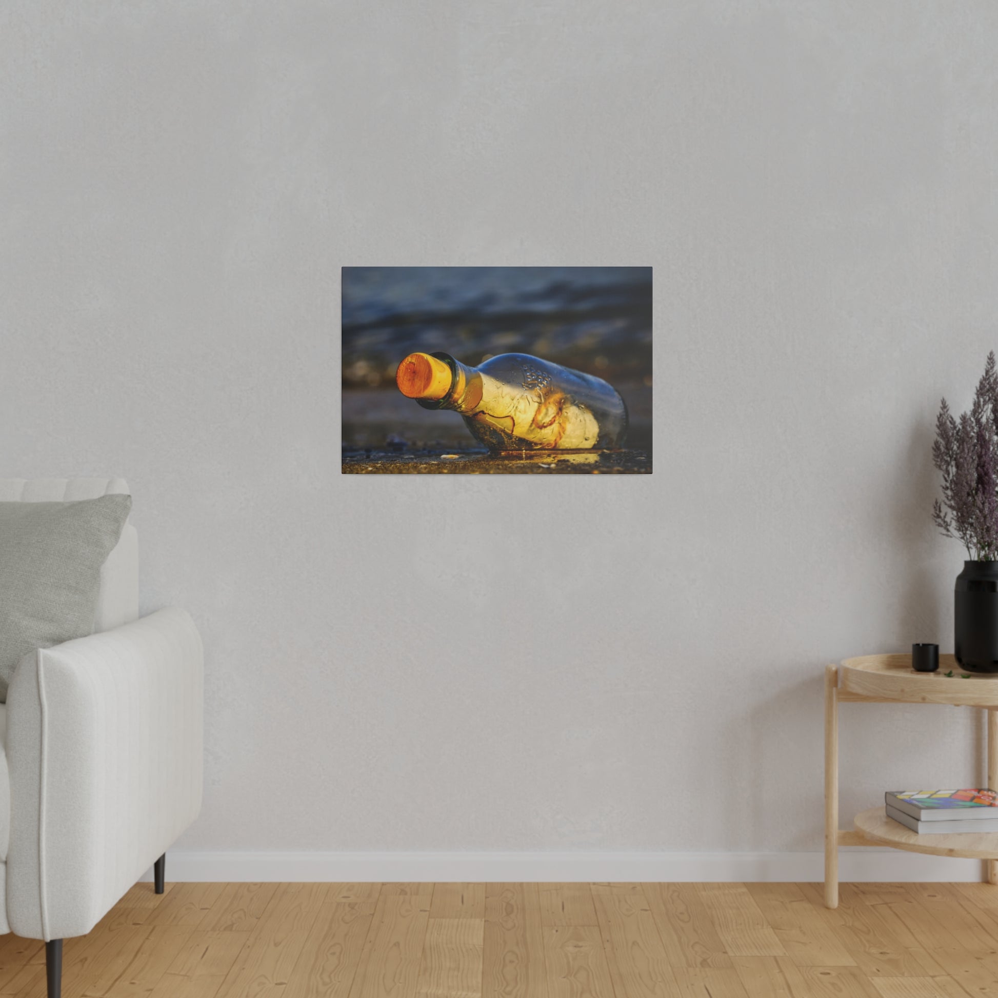 Small framed photo of a yellow glass bottle lying on a wet beach, hung on a light gray wall.