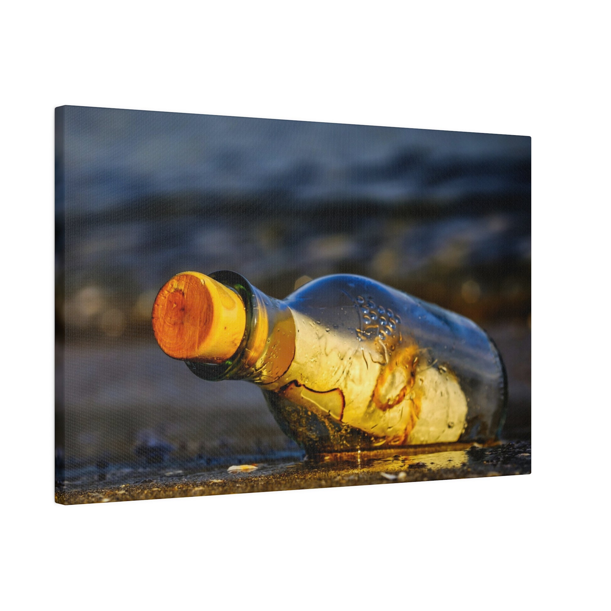 A clear glass bottle with an orange cap lies on its side on a wet, pebbled shore.