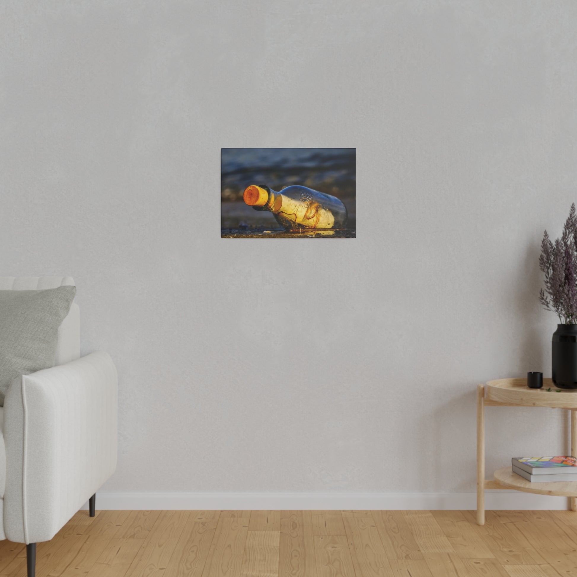 Small canvas print of a yellow-brown glass bottle lying on a sandy beach, mounted on a light gray living room wall.