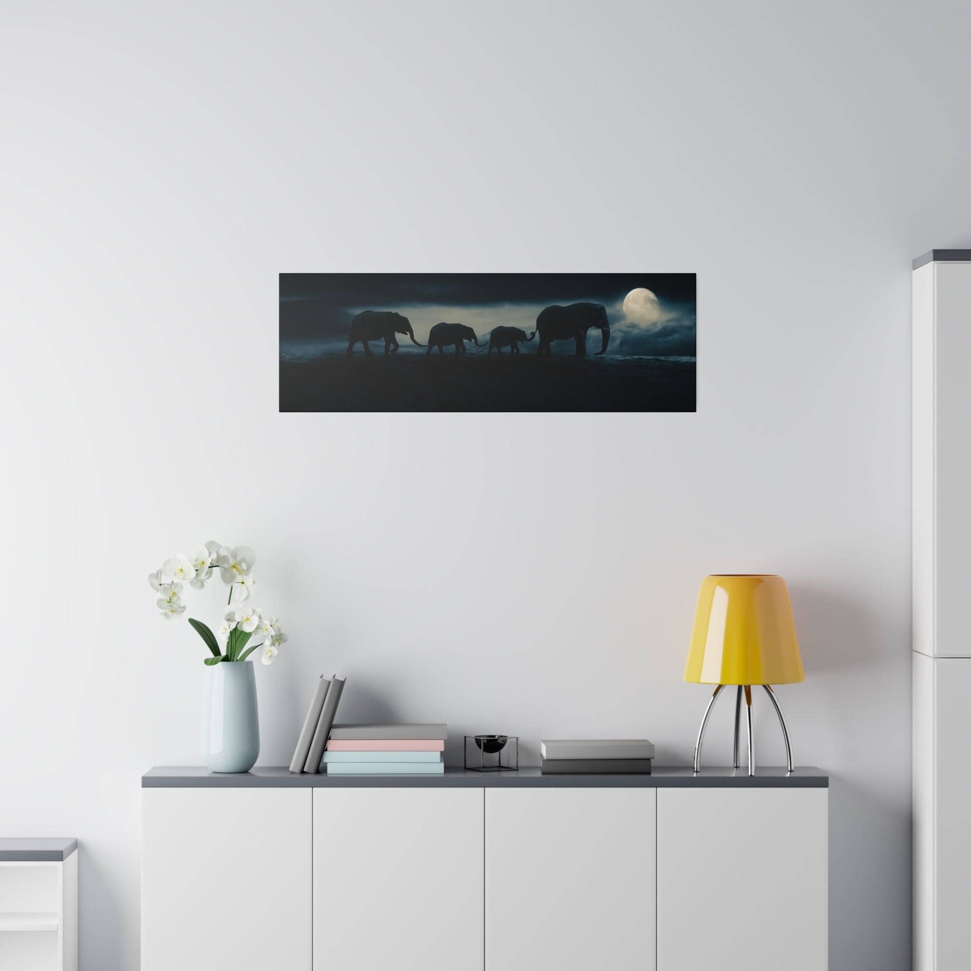 Panoramic wall art depicting silhouettes of five elephants walking at night under a moonlit sky.