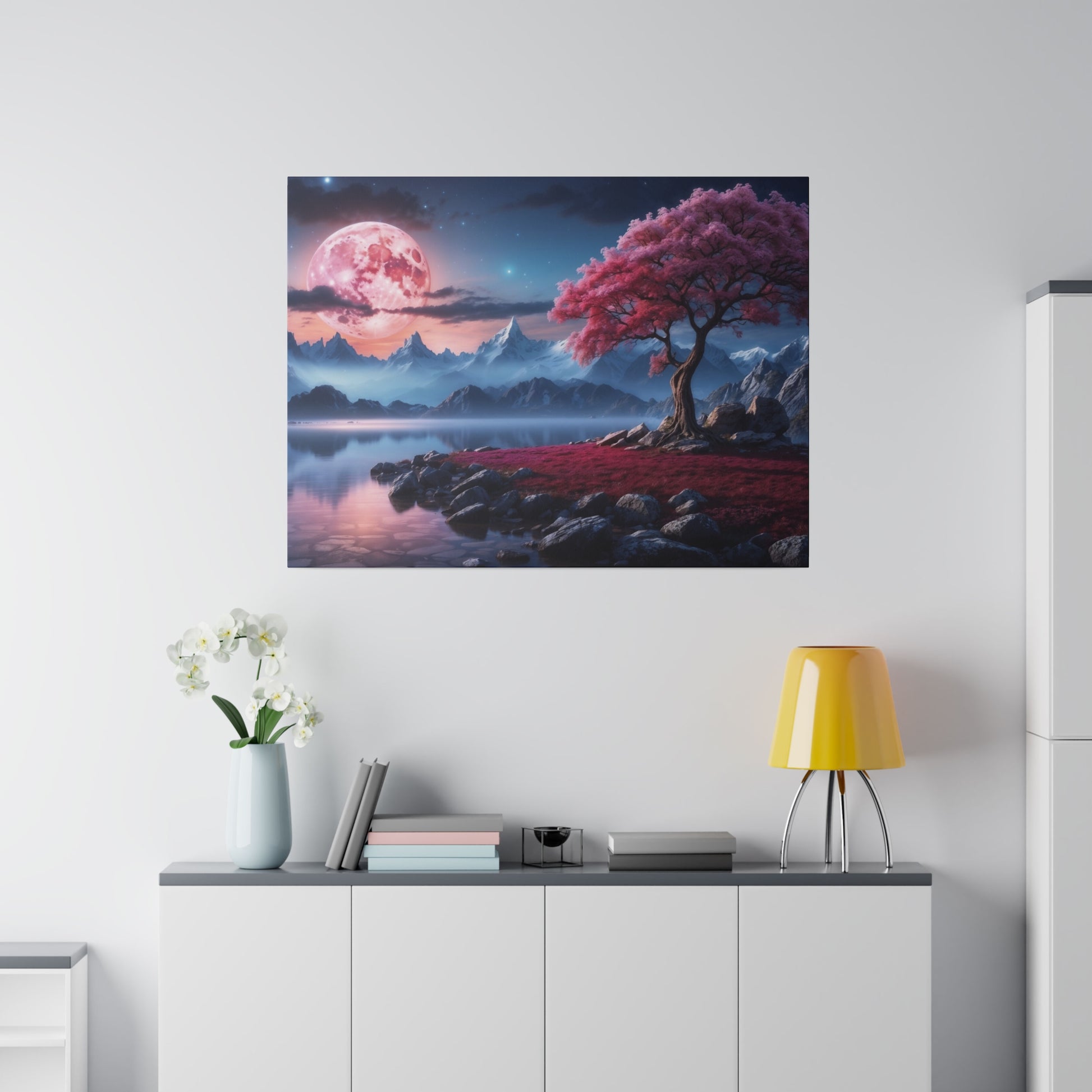 Square wall art showing a pink moon over blue mountains and a pink tree by a reflective lake with rocks.