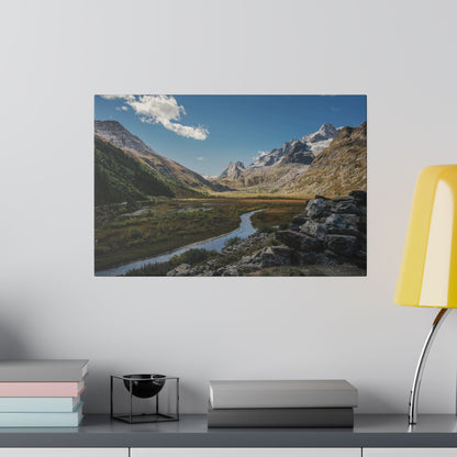 Landscape photo of a mountain valley with a winding river, rocky foreground, and snow-capped peaks under a blue sky.