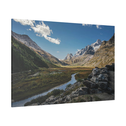Wide-angle landscape of a valley with a winding river, green slopes, and snow-capped mountains under a blue sky.