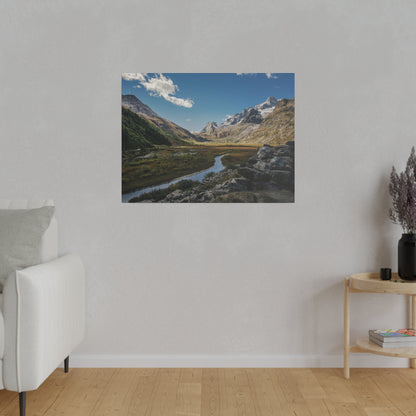 Framed landscape photo of a mountain valley with a winding river, snow-capped peaks, and a blue sky.
