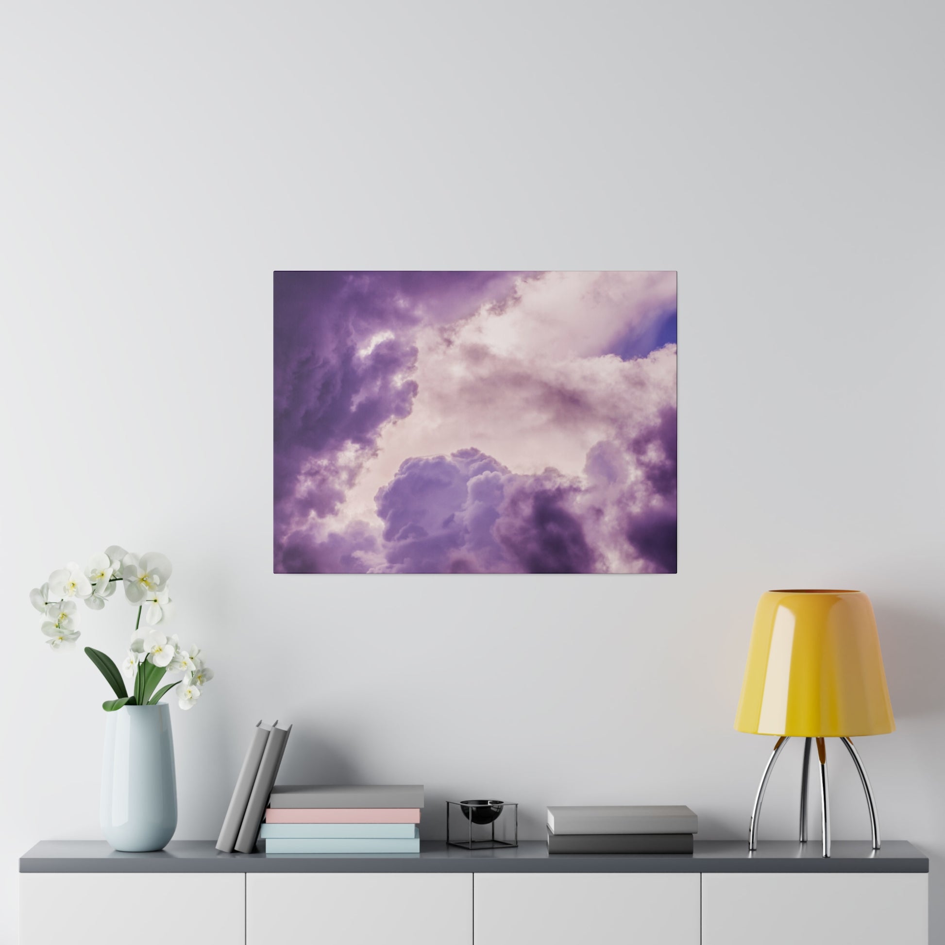 Square wall art print depicting a purple and lavender cloudy sky above a console with a light blue vase of white orchids, books, and a
