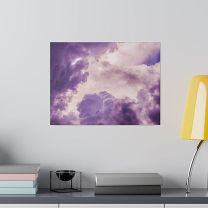 Square square wall art showing a purple-pink cloudy sky hangs above a gray desk with stacked books and a yellow lamp.