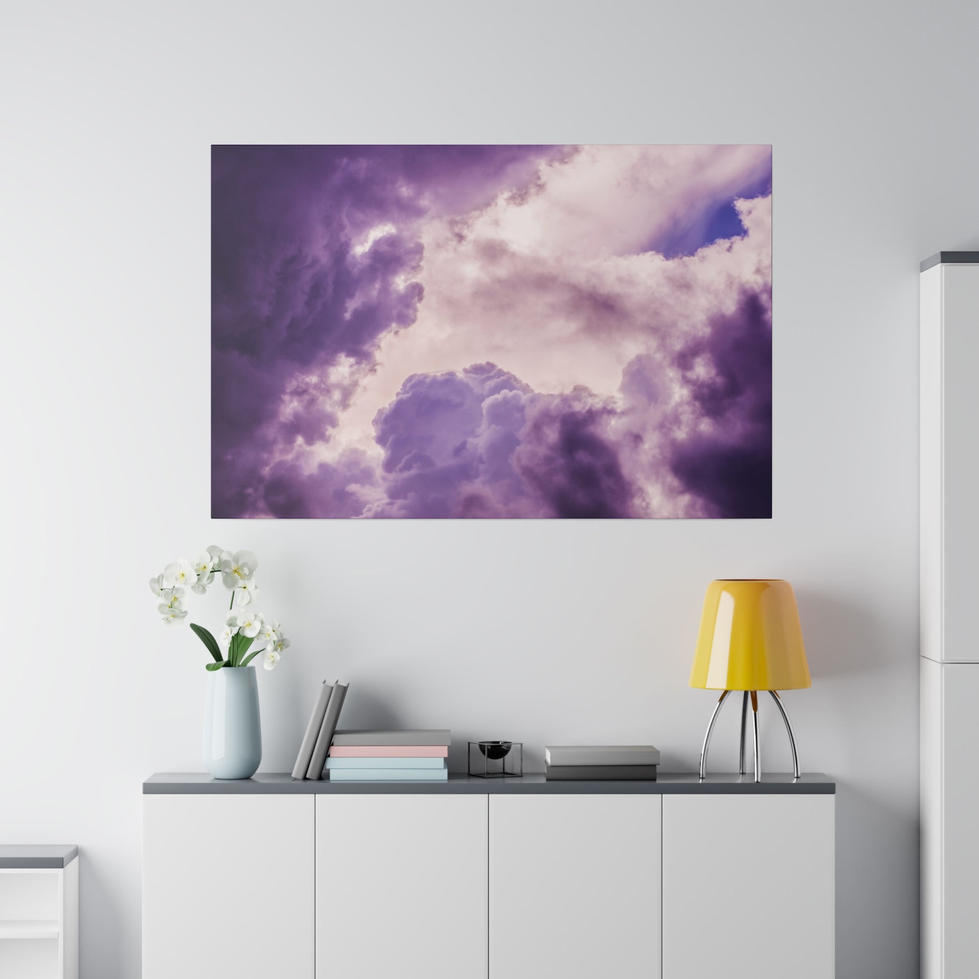 Large wall art showing purple and pink cloudscape against a bright sky, mounted above a white cabinet.