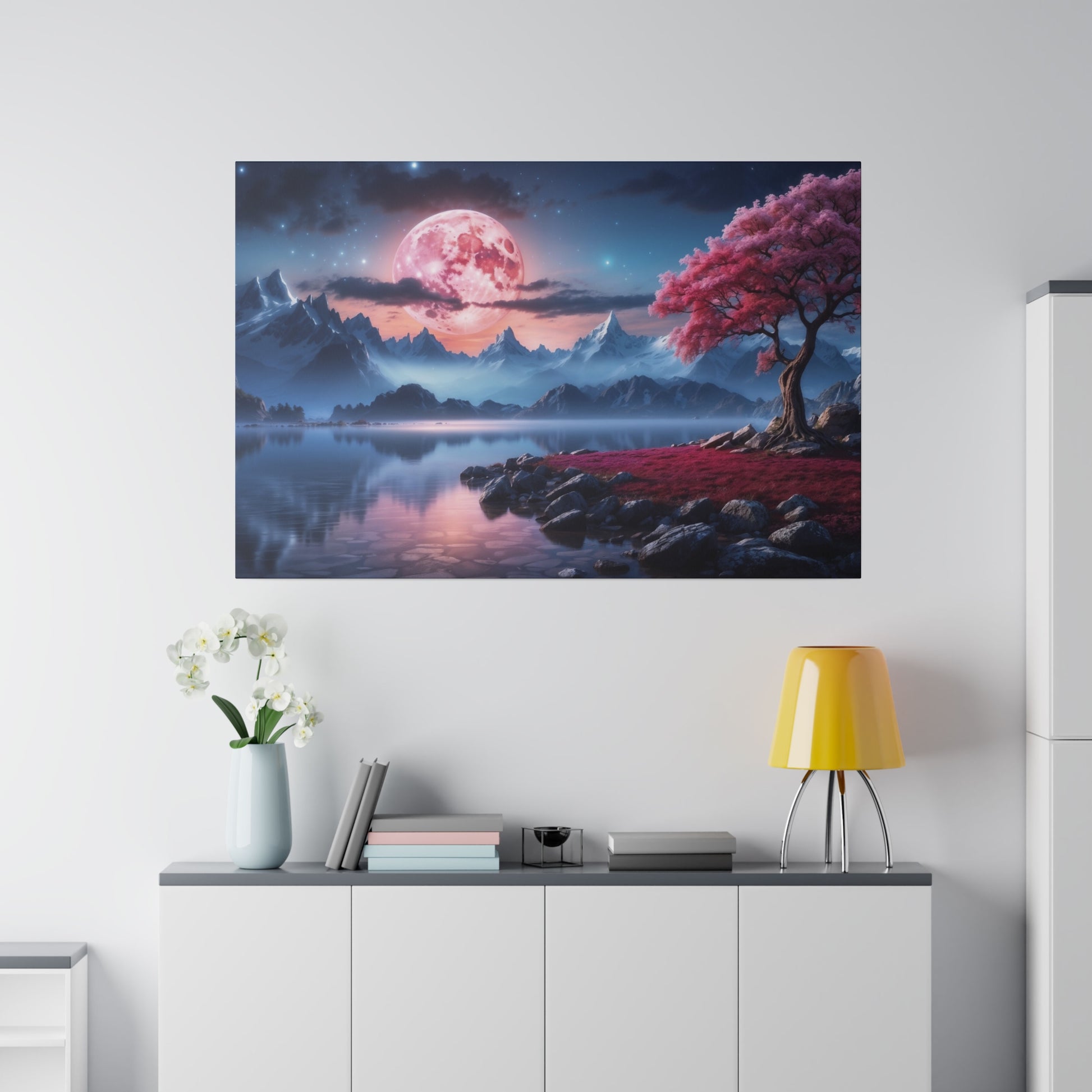 Framed wall art depicting a pink moon over blue mountains with a pink-leaved tree beside a calm lake.