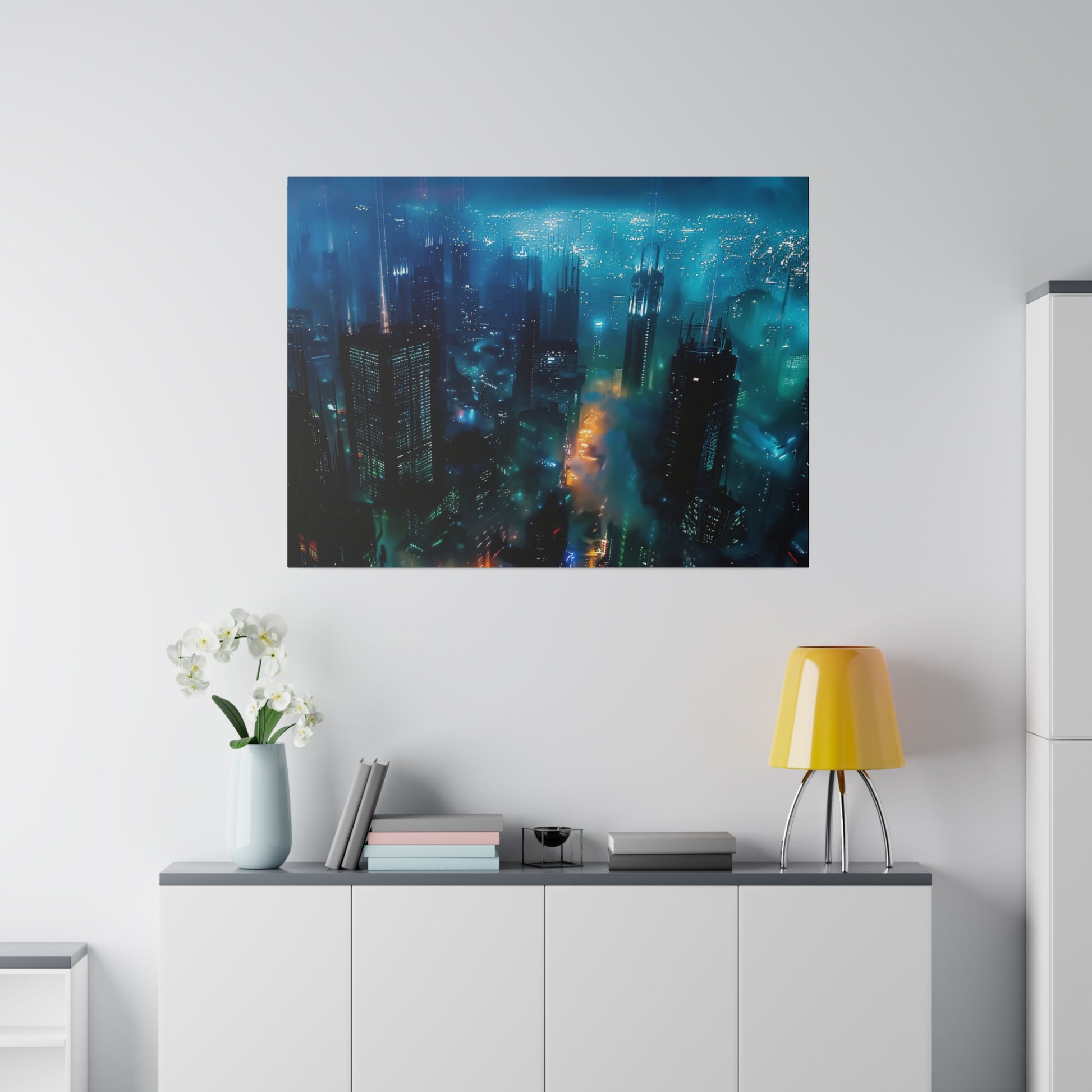 Framed blue cityscape photograph hanging above a white sideboard with a yellow lamp, vase of white flowers, and stacked books.