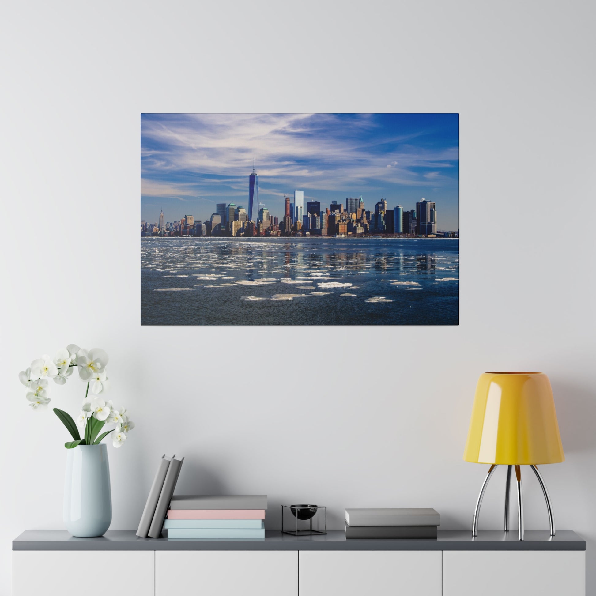 Daytime waterfront view of New York City, featuring the iconic skyline and patches of ice on the river surface.