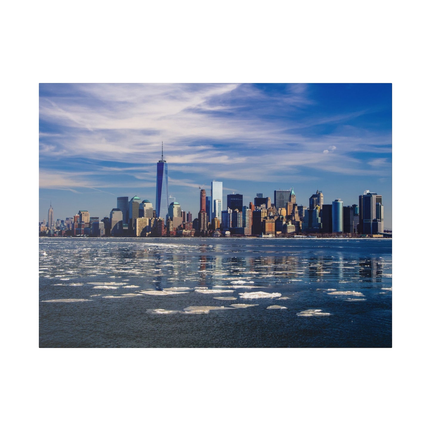 New York City skyscrapers as seen from the river, with patches of ice on the water and the skyline set against a blue sky.