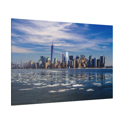 New York City skyline with tall buildings along a partially frozen river beneath a blue, partly cloudy sky.
