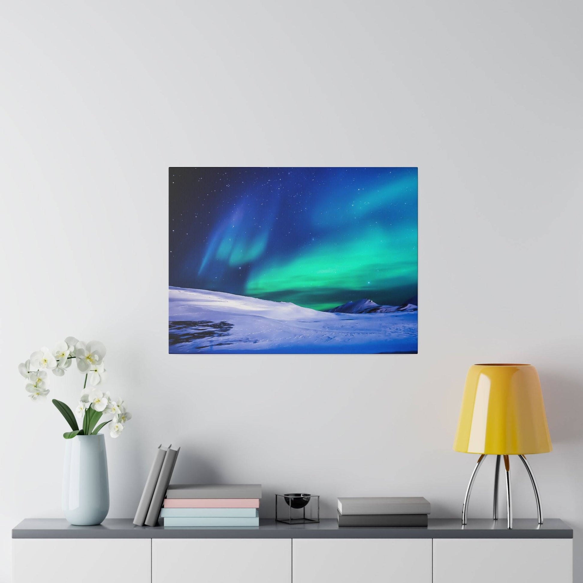 Square wall art depicting a snowy landscape with green and blue northern lights on a light gray wall.