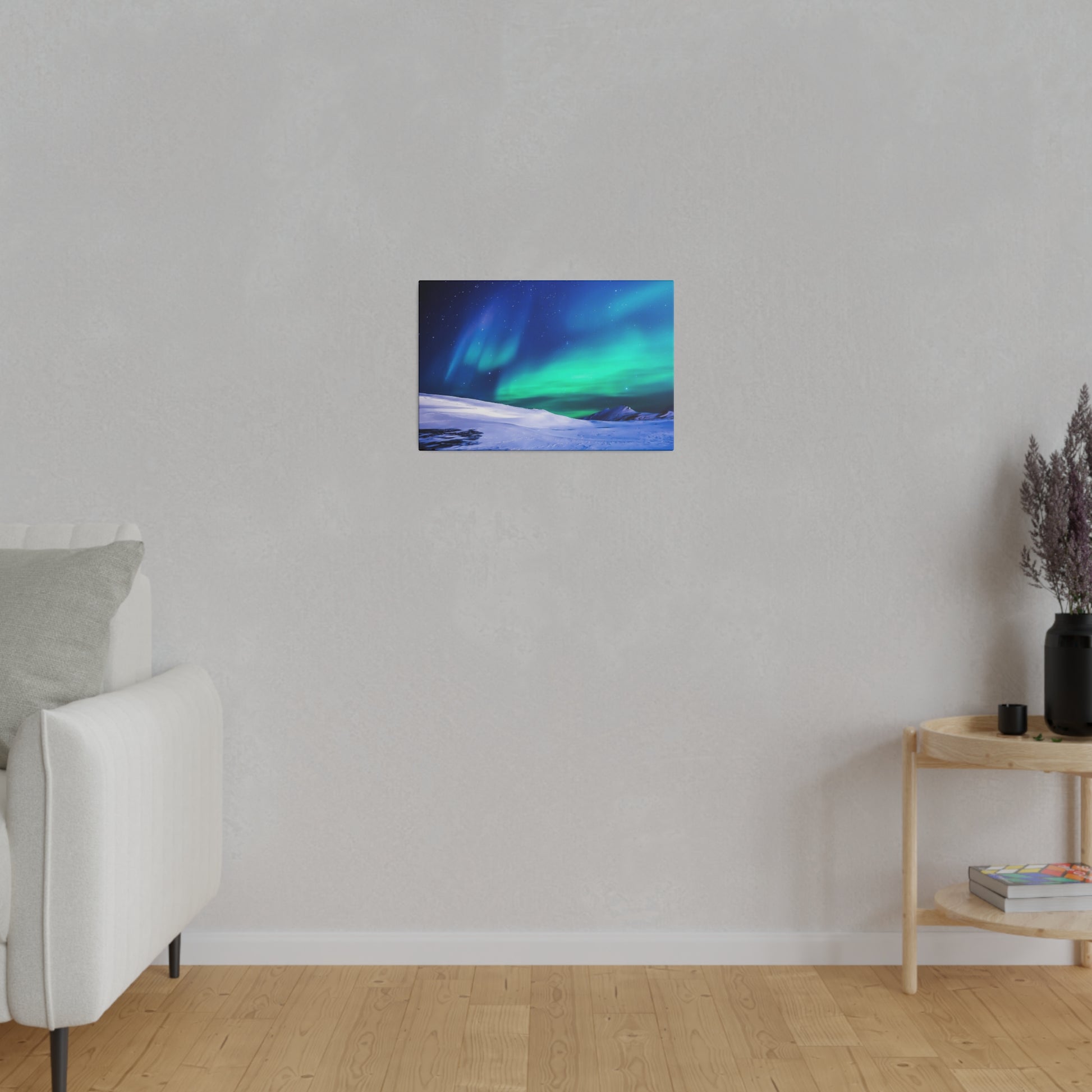Small rectangular canvas print of the blue-green aurora borealis over a snowy landscape, hung on a light gray wall in a minimalist living