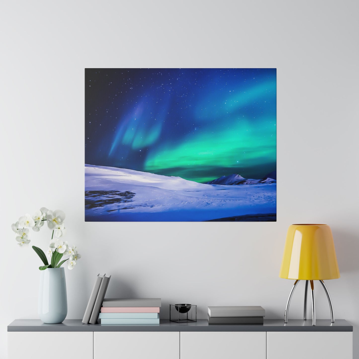 Square wall art depicting a night sky with green aurora over snow-covered hills, hung above a console with a yellow lamp.