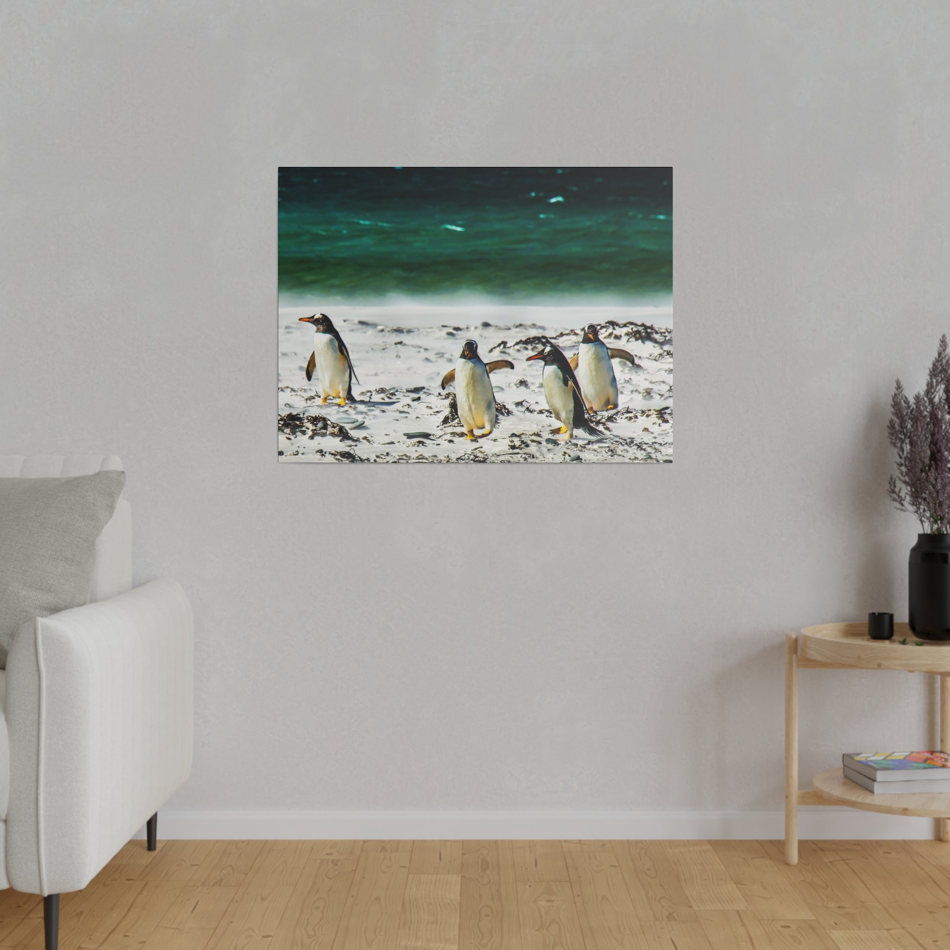 A group of penguins walking along a sandy beach near the ocean. The serene setting includes the waves of the sea and scattered seaweed.