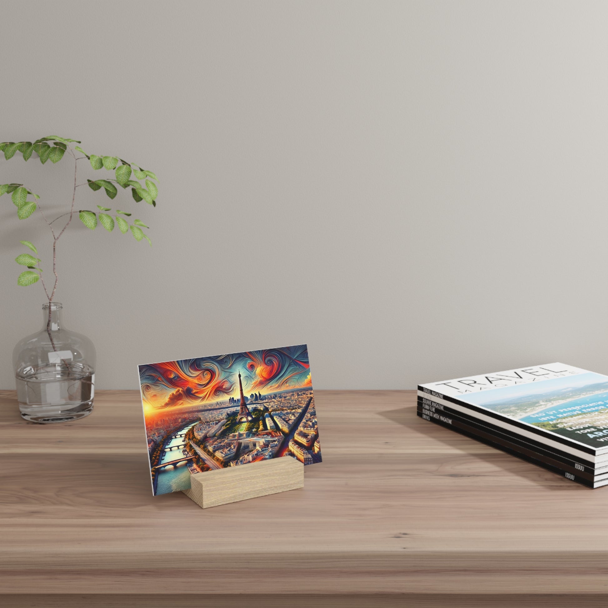 Colorful postcard of the Paris Eiffel Tower with a swirling orange-blue sky, propped on a light wood desk beside a glass vase and stacked