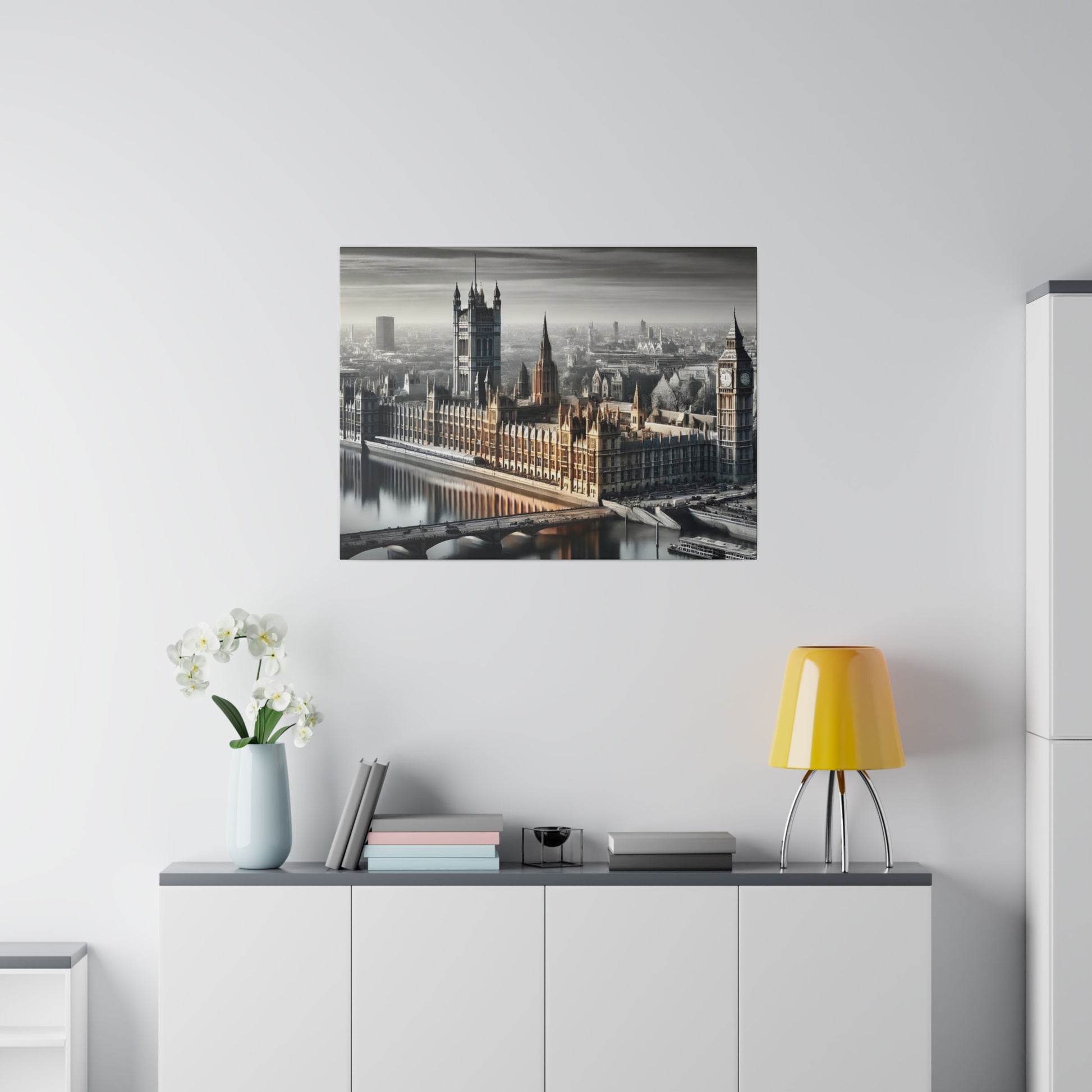 Framed grayscale photo of the Houses of Parliament and Westminster Bridge on a white wall above a white cabinet with a yellow lamp.