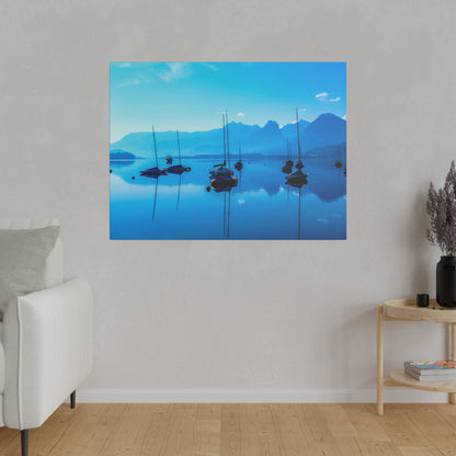 Framed blue-toned landscape photo of sailboats on calm lake with mountains in the background.