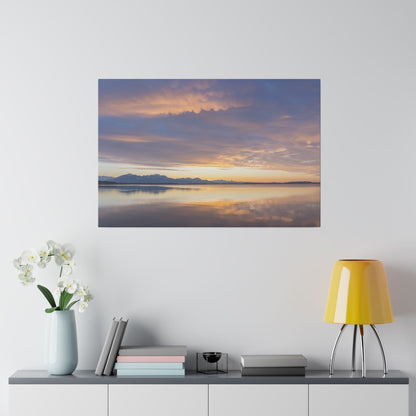 Framed landscape photo of a calm lake at sunset, with orange and purple sky and distant mountains reflected on the water.