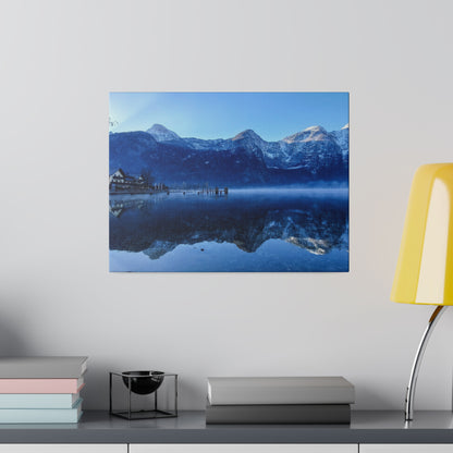 Snowy mountain range over a calm blue lake, with a small pier and cabin reflected on the water.