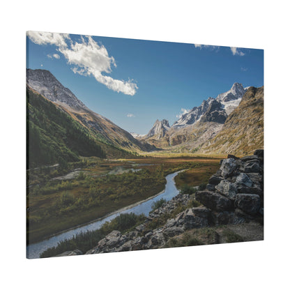 Snow-capped mountain valley with a winding river, green meadows, and a rocky foreground.
