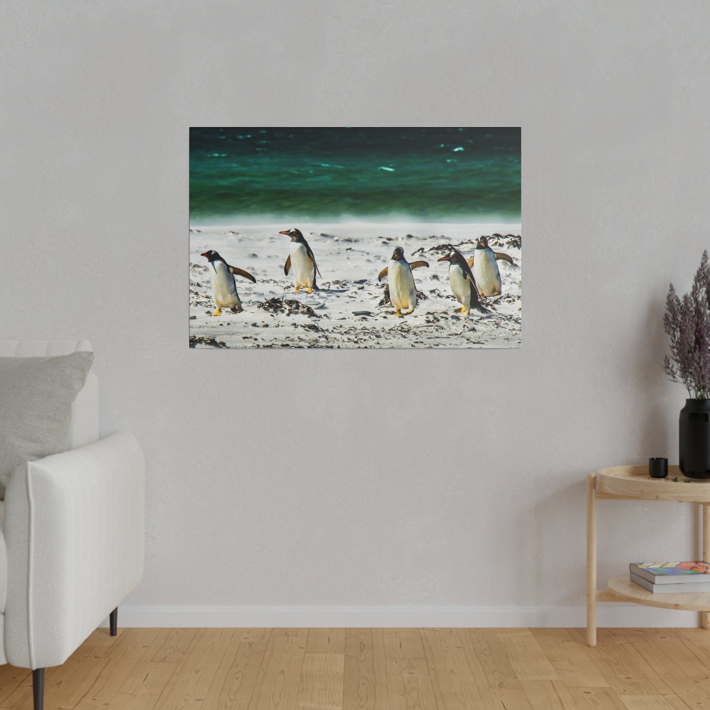 Penguins at the beachfront, with the ocean waves in the background. The sandy beach and seaweed create a tranquil setting for the penguins.