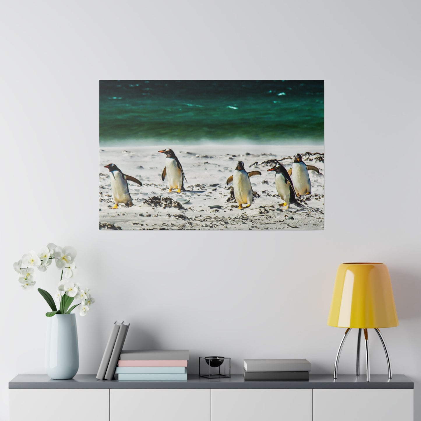 Penguins on a beach, with the ocean’s green-blue hues in the background. The white sand and seaweed create a tranquil seaside scene.