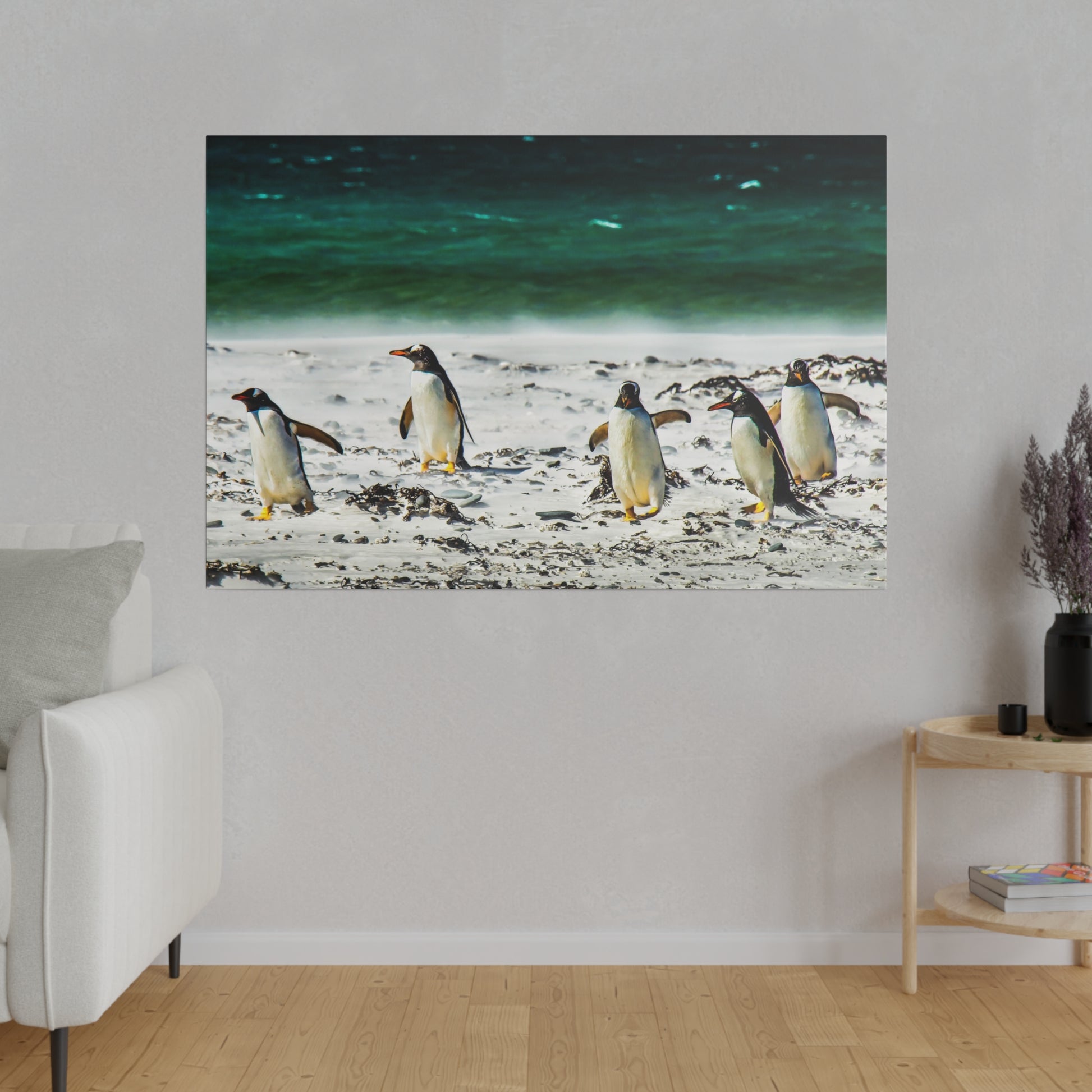 A group of penguins near the ocean, walking on a sandy beach. The green-blue sea provides a serene backdrop, with scattered seaweed adding to the natural setting.