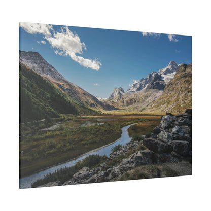Snow-capped jagged mountains overlook a grassy valley with a meandering river and rocky foreground.