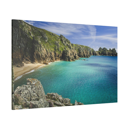 Rocky coastline with steep gray-brown cliffs, a small sandy beach, and clear turquoise sea under a blue sky.